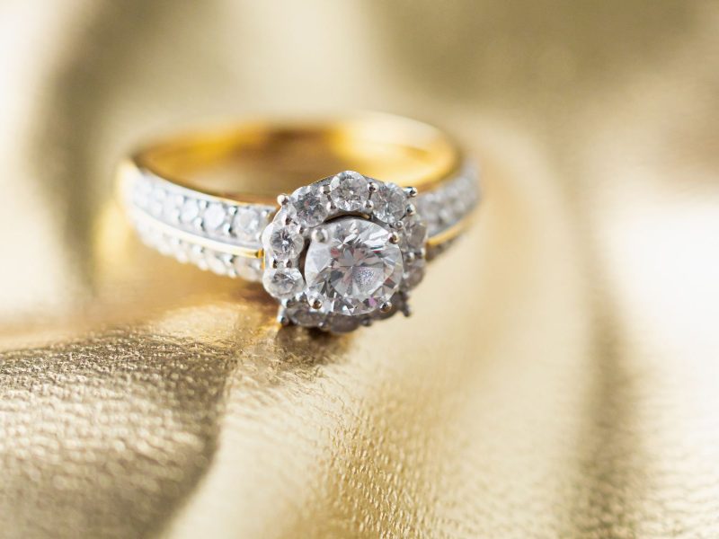 Custom engagement ring featuring a central diamond surrounded by smaller stones on a gold band against a golden background.