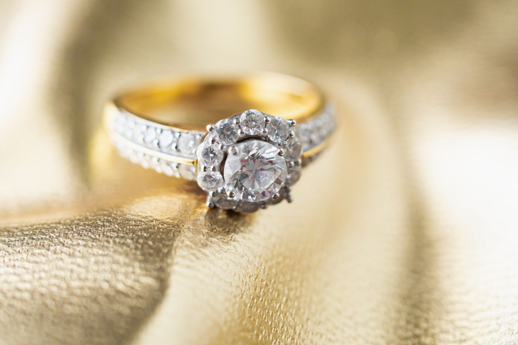 Custom engagement ring featuring a central diamond surrounded by smaller stones on a gold band against a golden background.