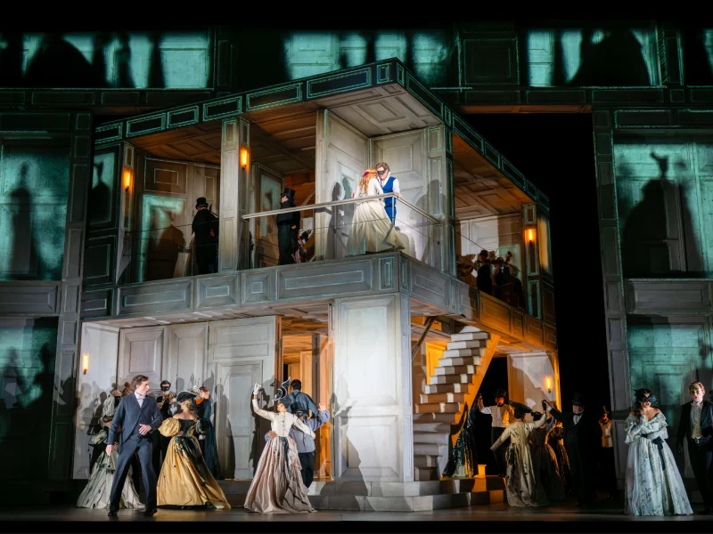 Scene from the Royal Opera’s Don Giovanni, showcasing actors in period costumes on a stylized set with dramatic lighting.