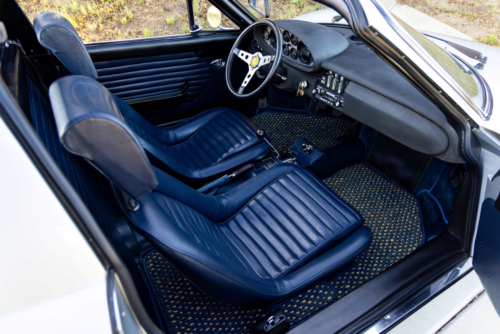 Interior view of a Ferrari Dino 246 GTS with blue leather seats and a dashboard showcasing classic controls.