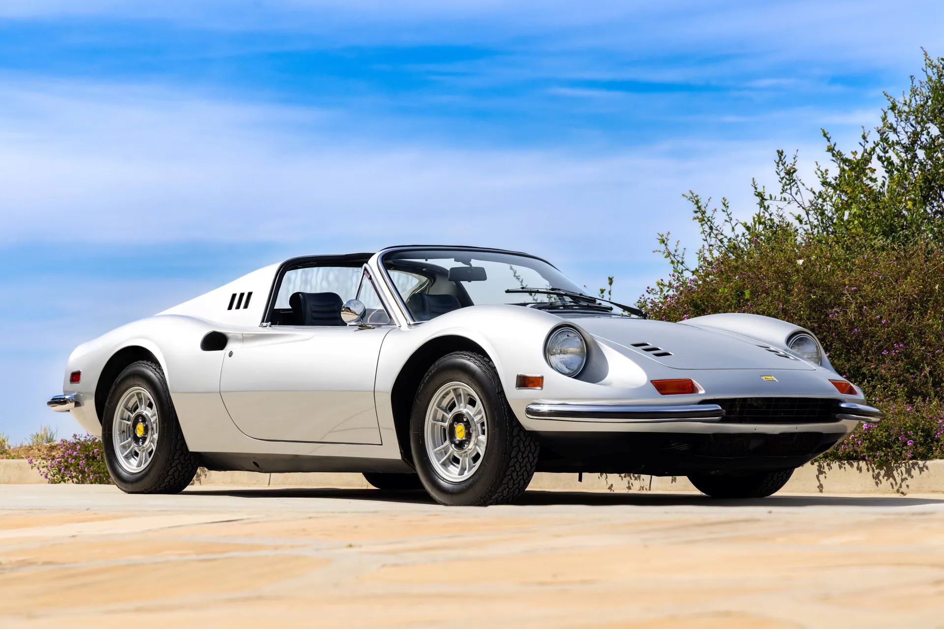 Ferrari Dino 246 GTS in white with black interior, shown at an outdoor location under a blue sky.