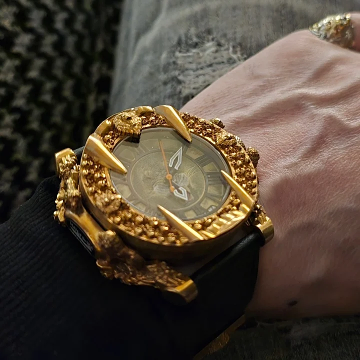 Golden watch with intricate design featuring sea-themed elements, worn on a wrist with a dark sleeve.