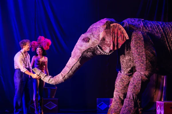 A performer and a male actor interact with a colorful elephant during a theatrical performance at the Pantages Theatre.