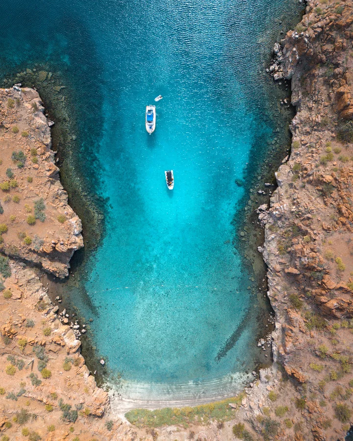 Turquoise water nestled between rocky cliffs with two boats anchored in a serene bay in Baja California Sur.