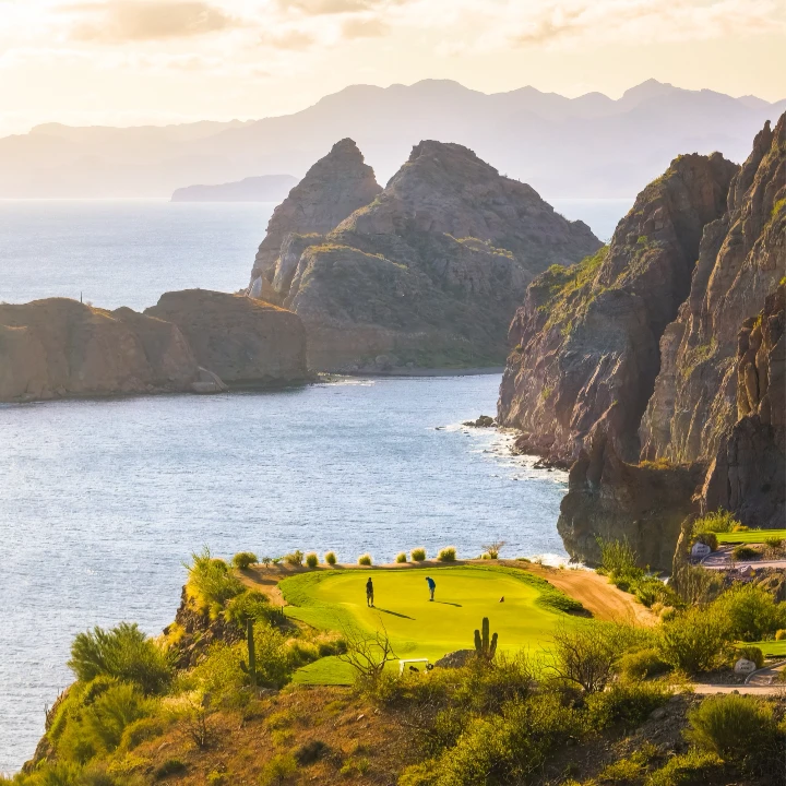 Scenic view of golfers on a green overlooking the ocean and rocky coastline at Danzante Bay, Baja California Sur.