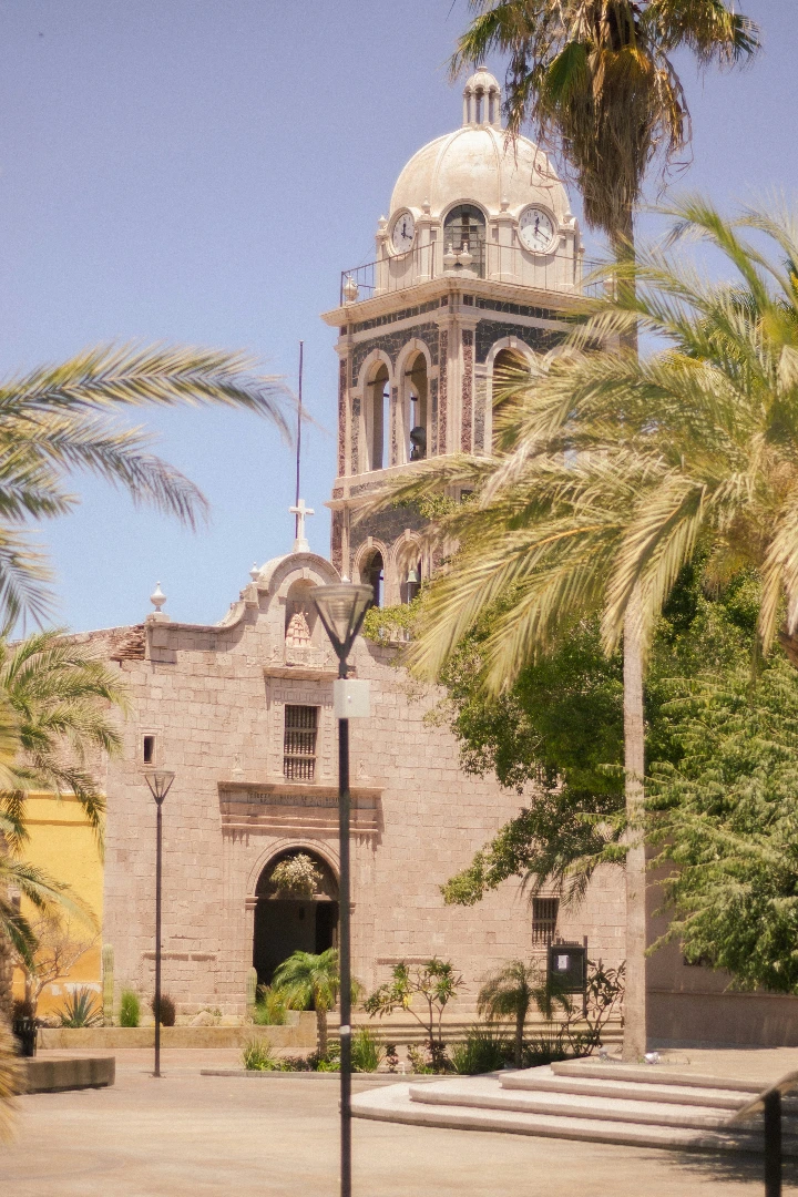 Historic church with a domed tower, surrounded by palm trees and a vibrant plaza in Loreto, Baja California Sur.
