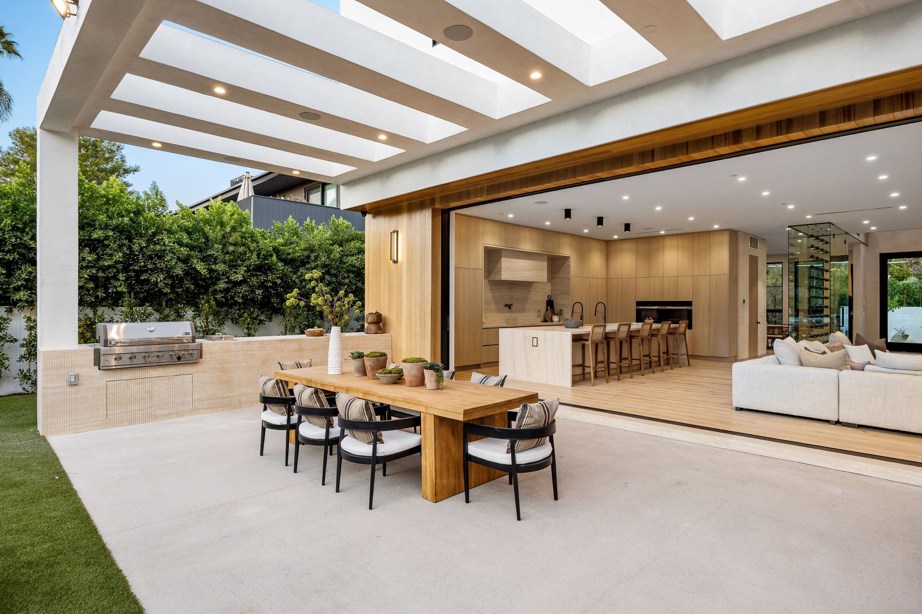 Modern outdoor dining area featuring a wooden table, stylish chairs, and a built-in grill, seamlessly connected to a spacious interior.