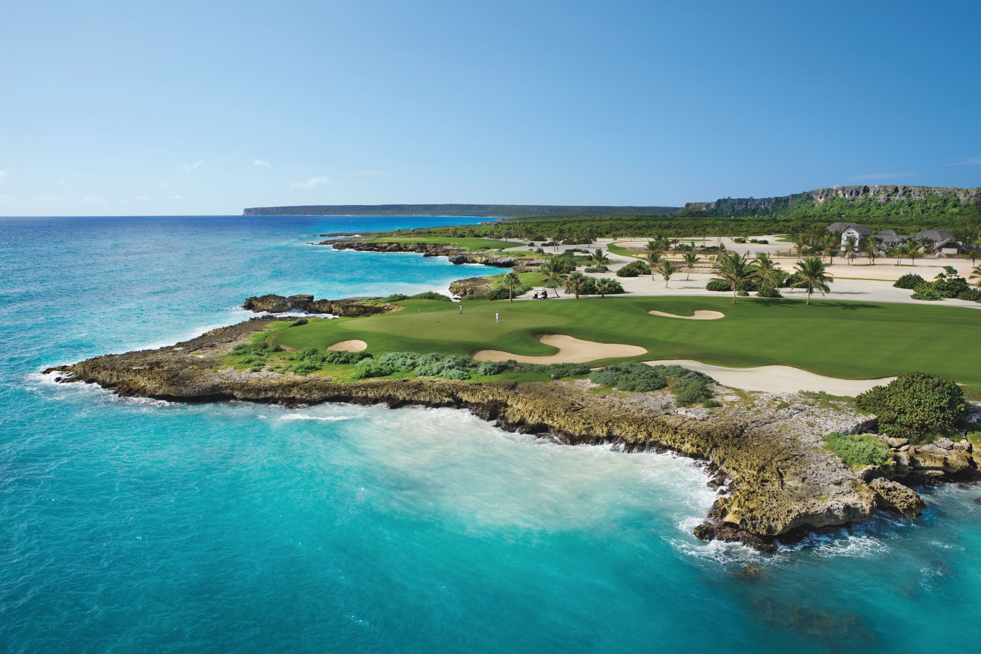 Coastal view of The St. Regis Cap Cana Resort featuring a golf course, turquoise waters, and rocky shorelines.