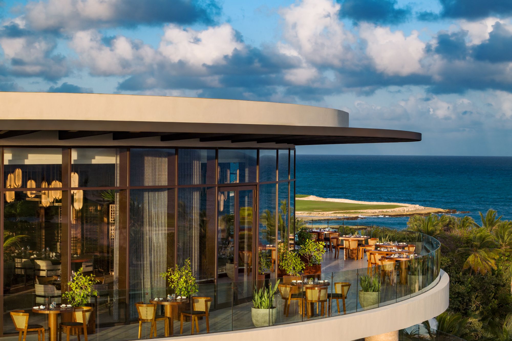 A modern restaurant terrace overlooking the ocean at The St. Regis Cap Cana Resort, surrounded by palm trees and blue skies.