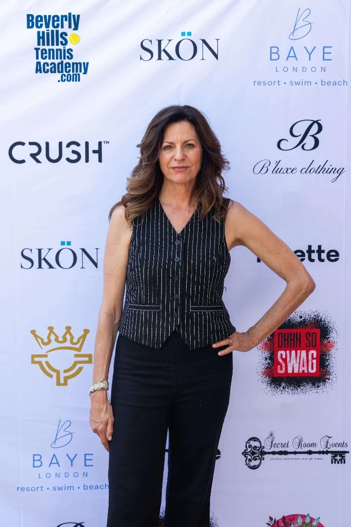 Woman in a striped vest stands confidently at a branded event backdrop with multiple logos.