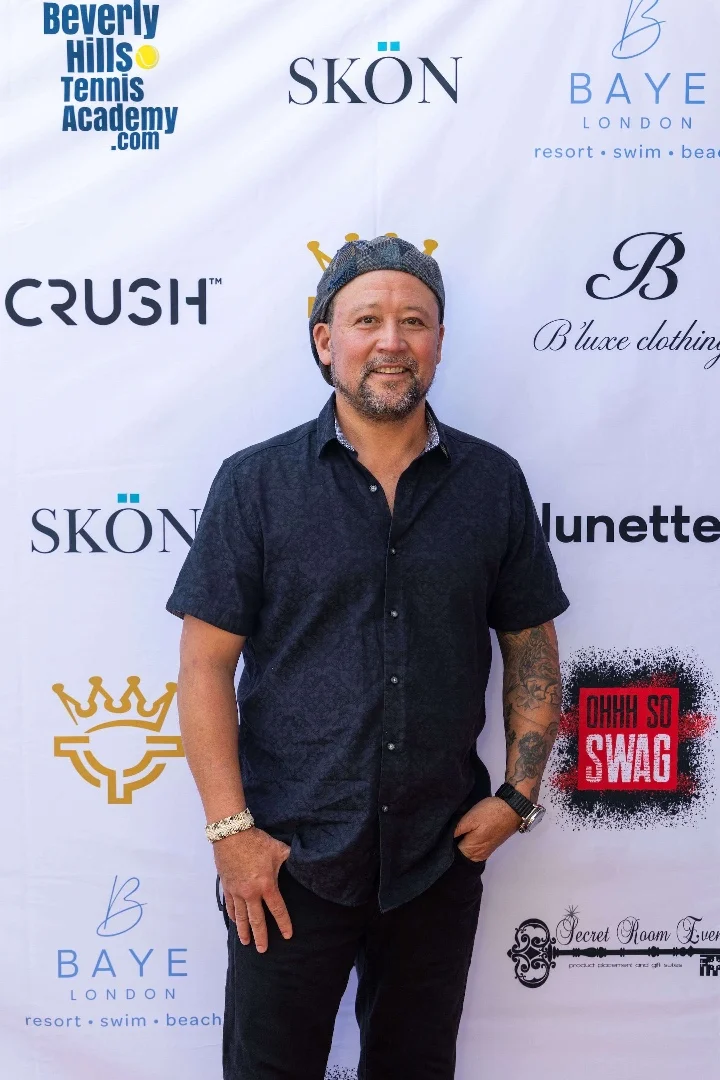 Man in a black shirt poses at a promotional event backdrop featuring various brand logos and the Secret Room Events branding.