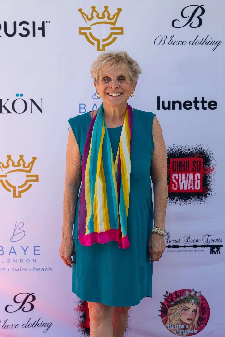 A smiling woman wearing a teal dress and colorful scarf poses at a red carpet event for the Celebrity Prime Time Emmy Nominees.