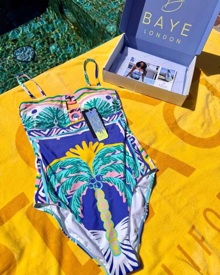 Baye London swimsuit featuring vibrant tropical design and packaging displayed on a bright yellow towel by a pool.