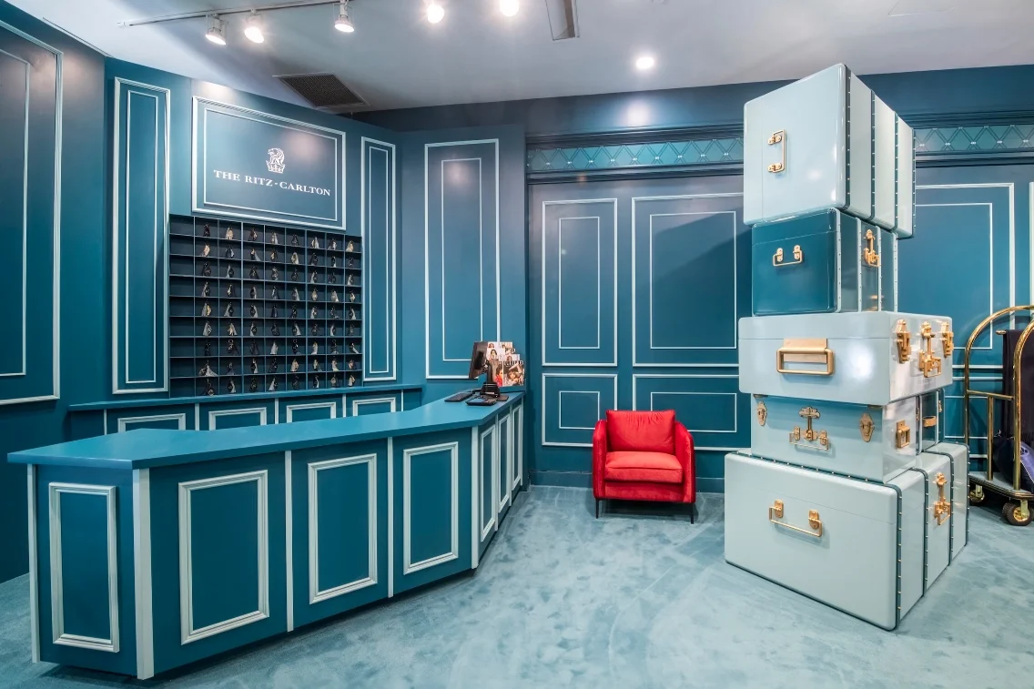 Ritz-Carlton styled reception area featuring a turquoise desk, wall-mounted key display, and stacked vintage suitcases.