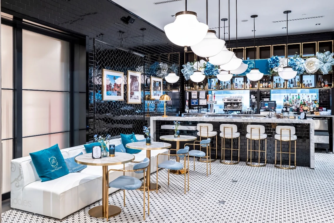 Stylish interior of a bar area with marble tables, gold accents, and floral decor at Bloomingdale’s for The Ritz-Carlton.