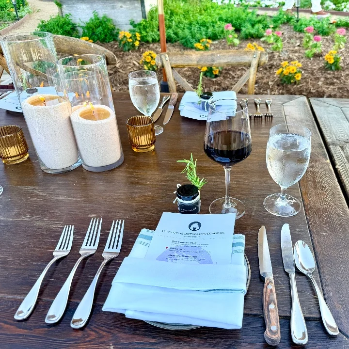Table set for a dinner with candles, wine, glasses of water, cutlery, and a menu, surrounded by colorful flowers at Temecula Creek Inn.