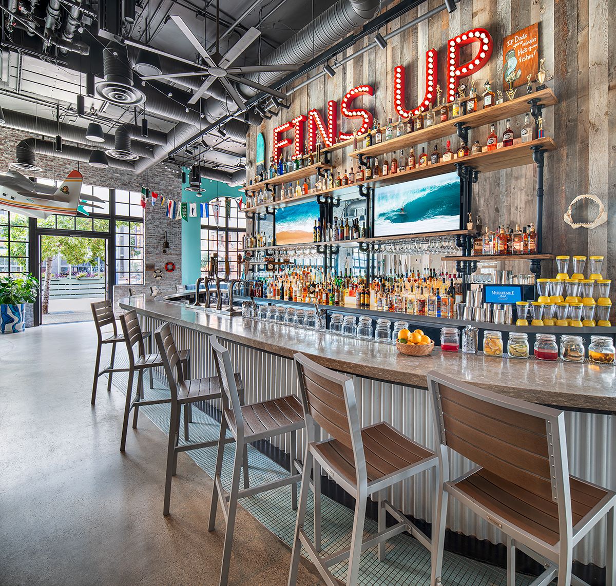 Bar area featuring a long countertop, colorful bottle display, and bright "Fins Up" sign in a lively setting.