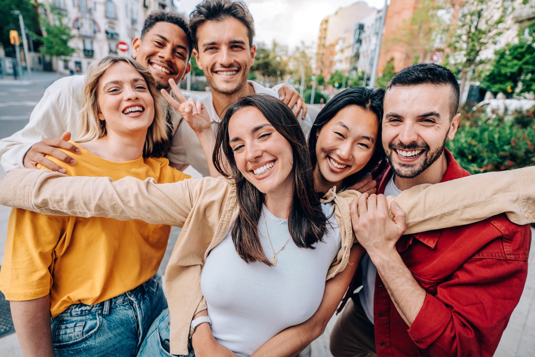 A diverse group of six friends smiling and posing together outdoors, conveying joy and connection.