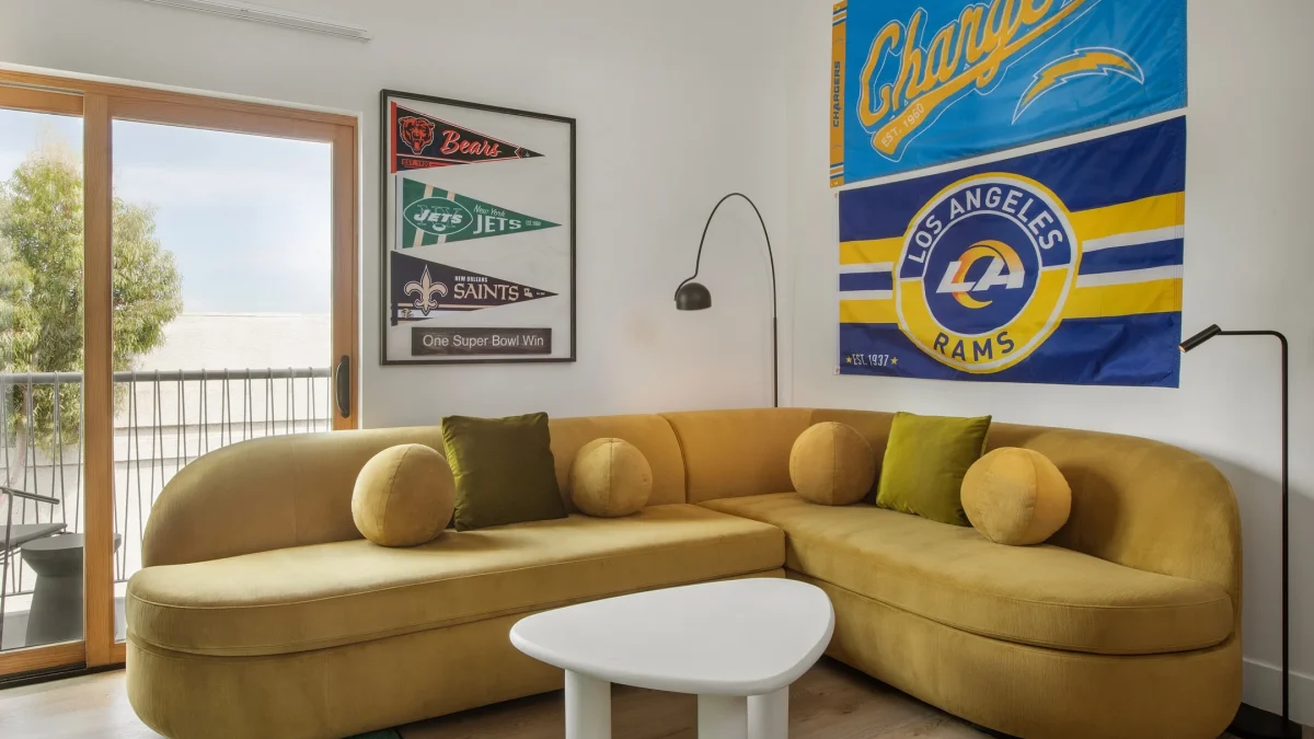 Cozy football-themed suite featuring a yellow curved sofa, team pennants, and a balcony view at the Anthem Hotel.