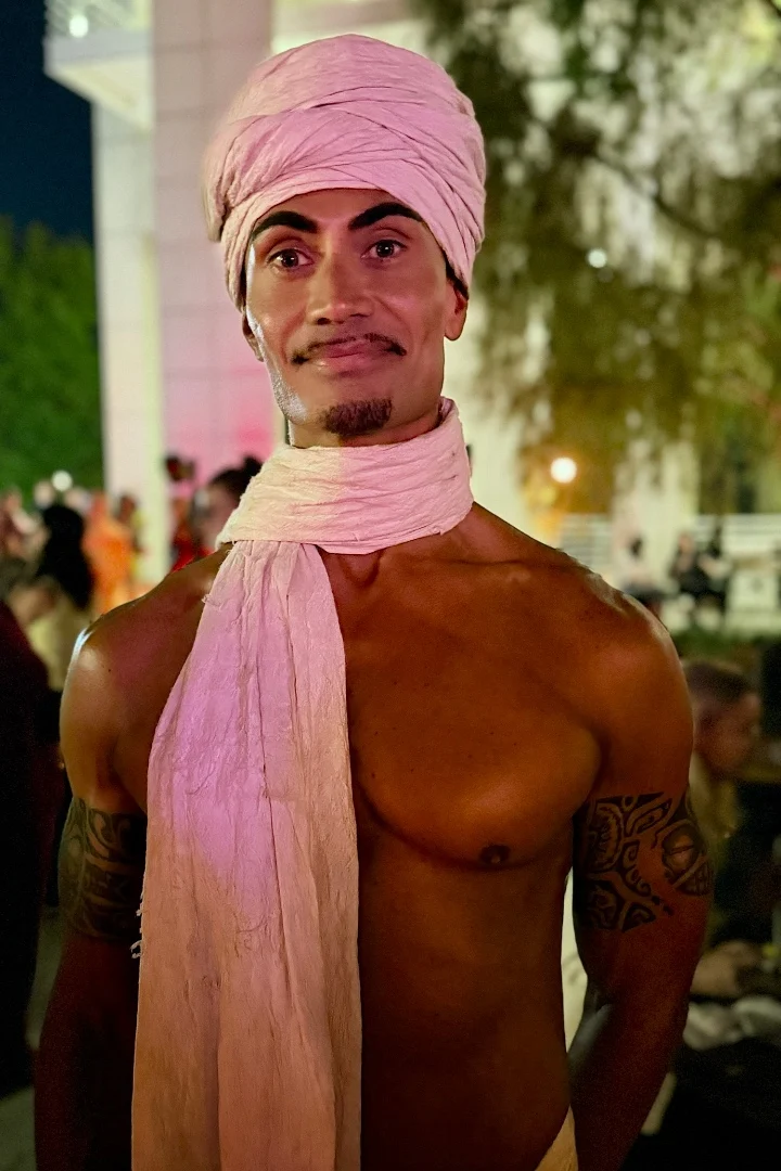 Man wearing a light fabric turban and scarf, posing confidently at an outdoor event.