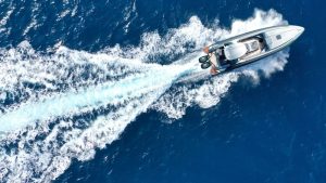 A luxury motor yacht glides through deep blue waters, leaving a trail of white frothy waves behind.