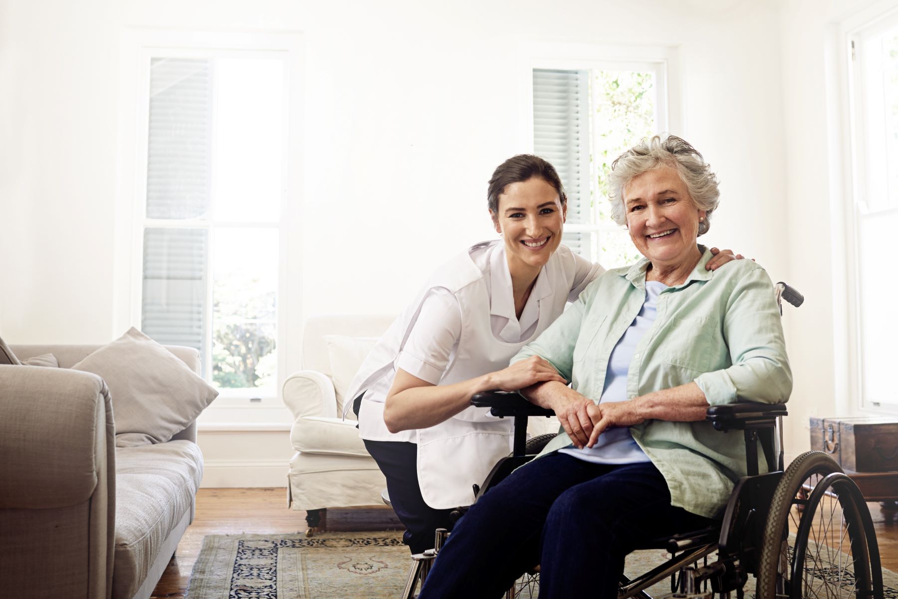 A caregiver and a senior woman smile together in a bright, comfortable living space, promoting a supportive homecare environment.
