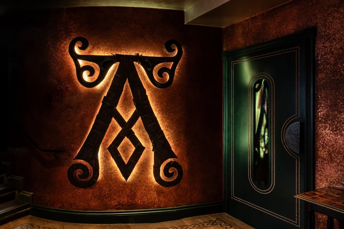 Illuminated A-shaped logo on a textured wall beside a decorative green door in Ardbeg House, Islay.