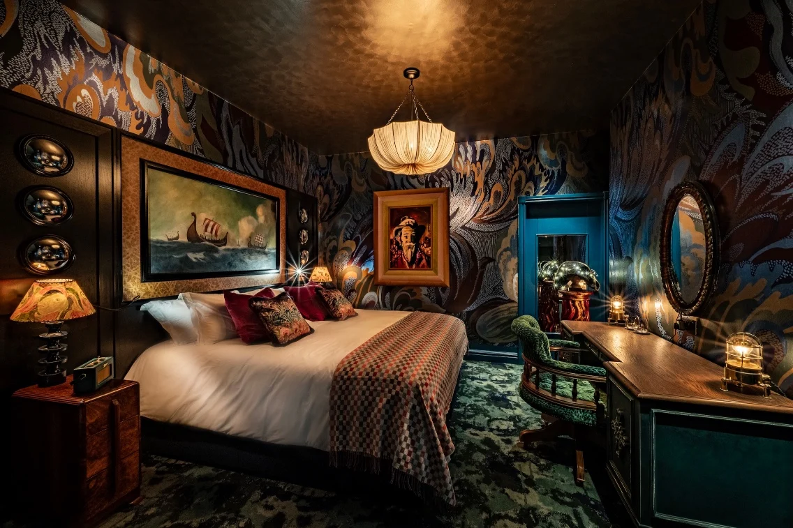Luxurious bedroom with intricate wallpaper, a cozy bed, decorative lamps, and artistic elements in a stylish setting.