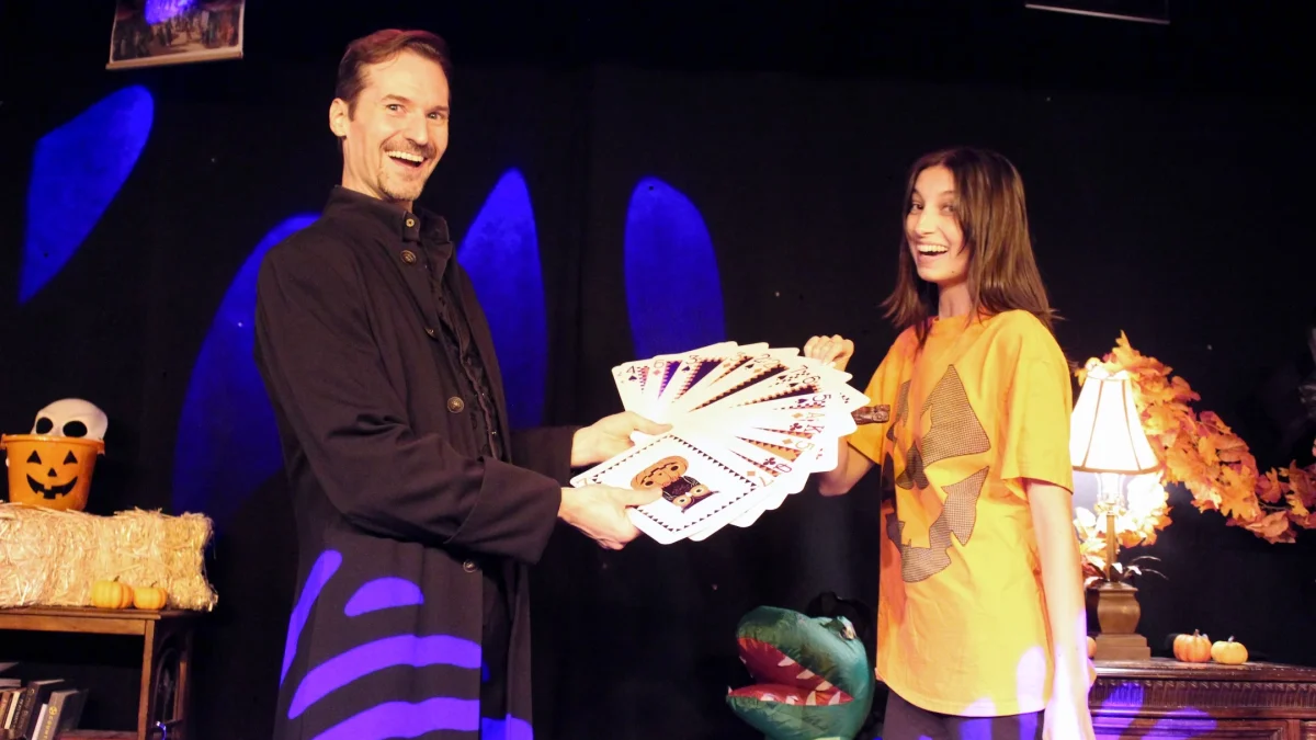 A magician shares a colorful deck of cards with a smiling assistant during a Halloween-themed performance at WonderWorks Orlando.