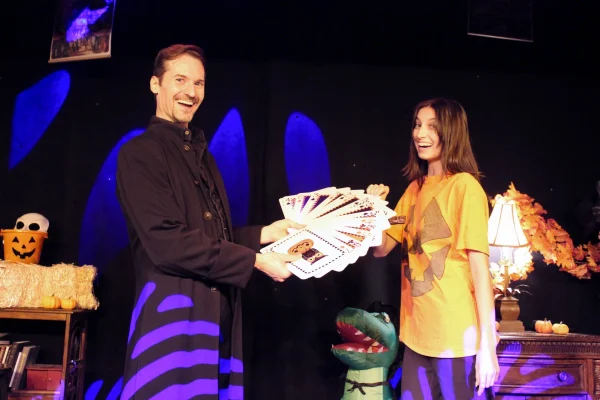 A magician shares a colorful deck of cards with a smiling assistant during a Halloween-themed performance at WonderWorks Orlando.