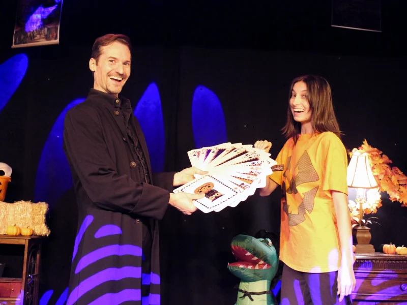 A magician shares a colorful deck of cards with a smiling assistant during a Halloween-themed performance at WonderWorks Orlando.