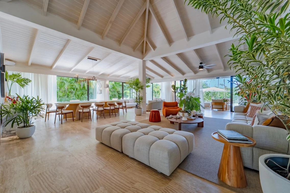 Stylish living area featuring a large dining table, cozy seating, and greenery, highlighting a serene indoor-outdoor feel.