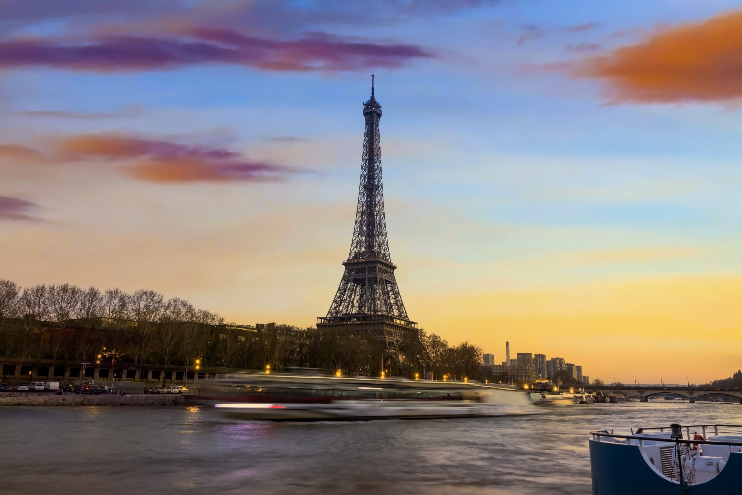Eiffel Tower at sunset with a riverboat passing along the Seine, showcasing the beauty of Paris.