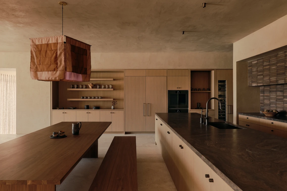 Minimalist kitchen design featuring a large wooden table, modern cabinetry, and a unique hanging light fixture.