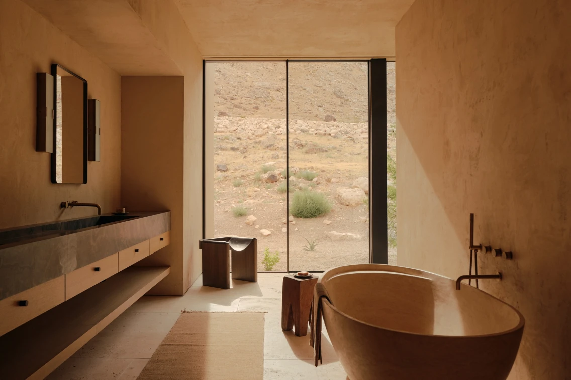 Sleek desert retreat bathroom featuring a stone sink, modern tub, and large window overlooking the natural landscape.