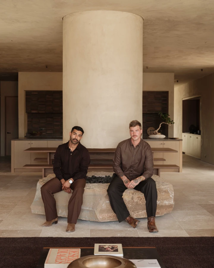 Two men seated on a stone bench in a modern interior, featuring a large column and minimalist decor.