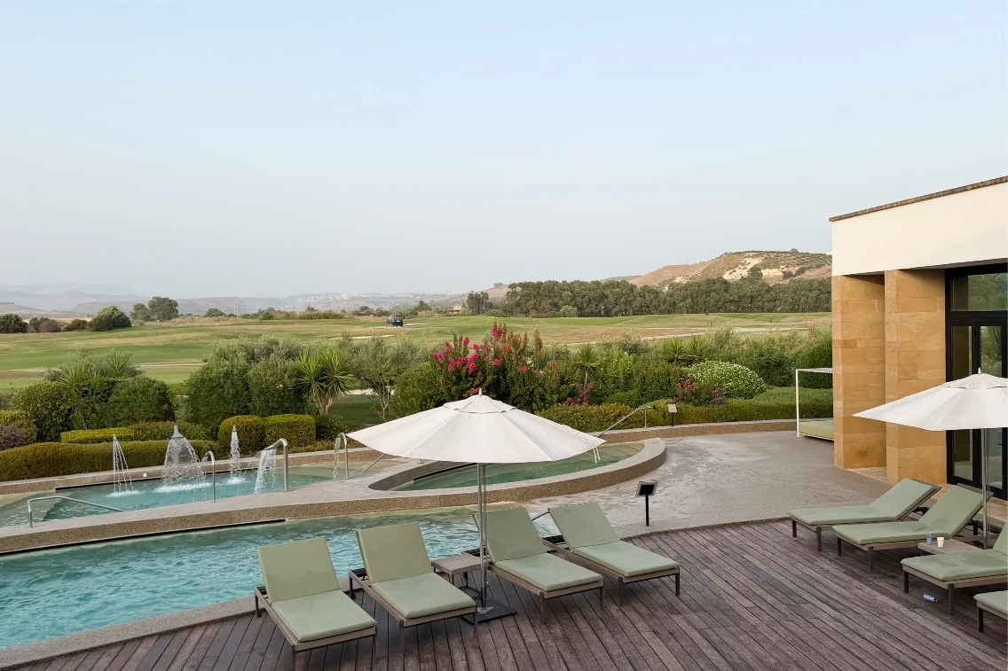Poolside lounge chairs overlook a serene landscape at Rocco Forte’s Verdura Resort, blending spa luxury with natural beauty.