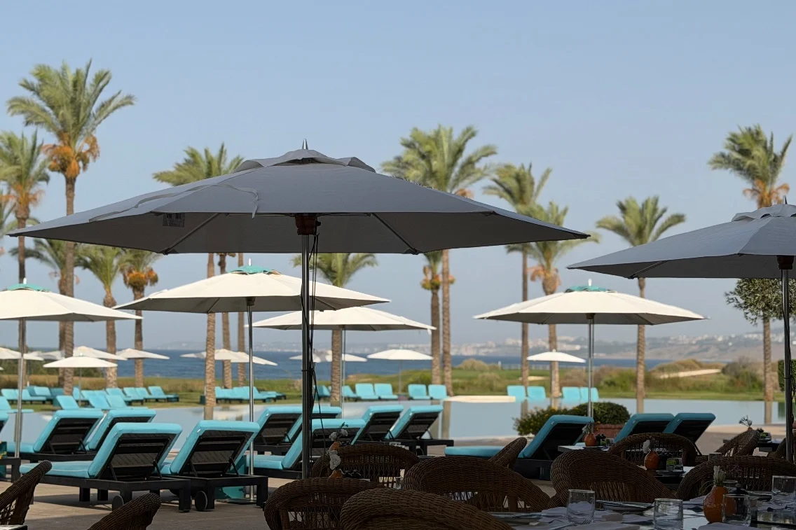 Loungers and umbrellas line the pool area at Rocco Forte’s Verdura Resort, with palm trees and the sea in the background.