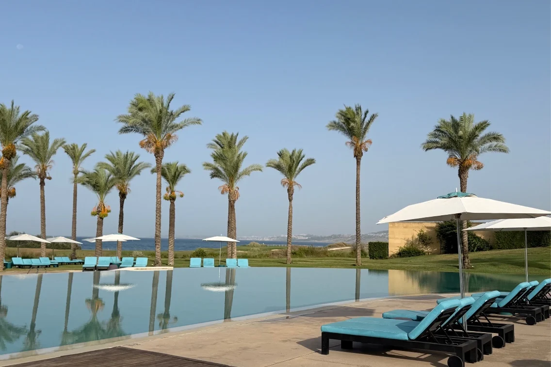 A serene pool area at Rocco Forte’s Verdura Resort, surrounded by palm trees and overlooking the sea.