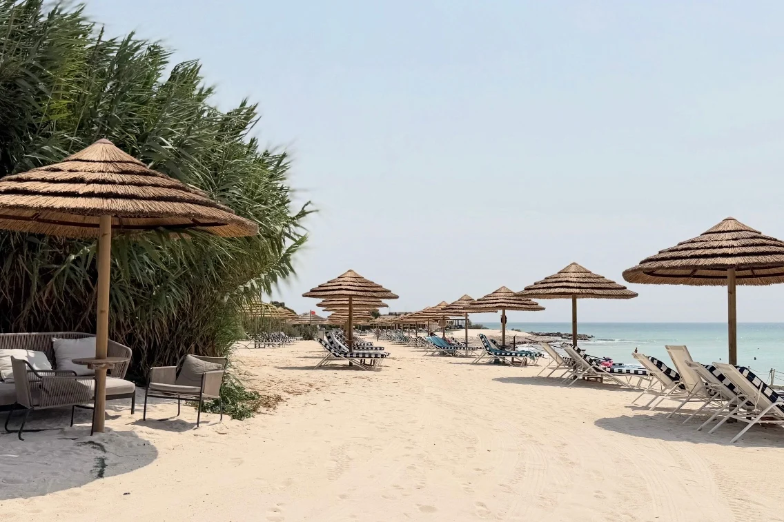 Beached umbrellas and lounge chairs line the sandy shore, offering relaxation near the tranquil sea at Rocco Forte’s Verdura Resort.