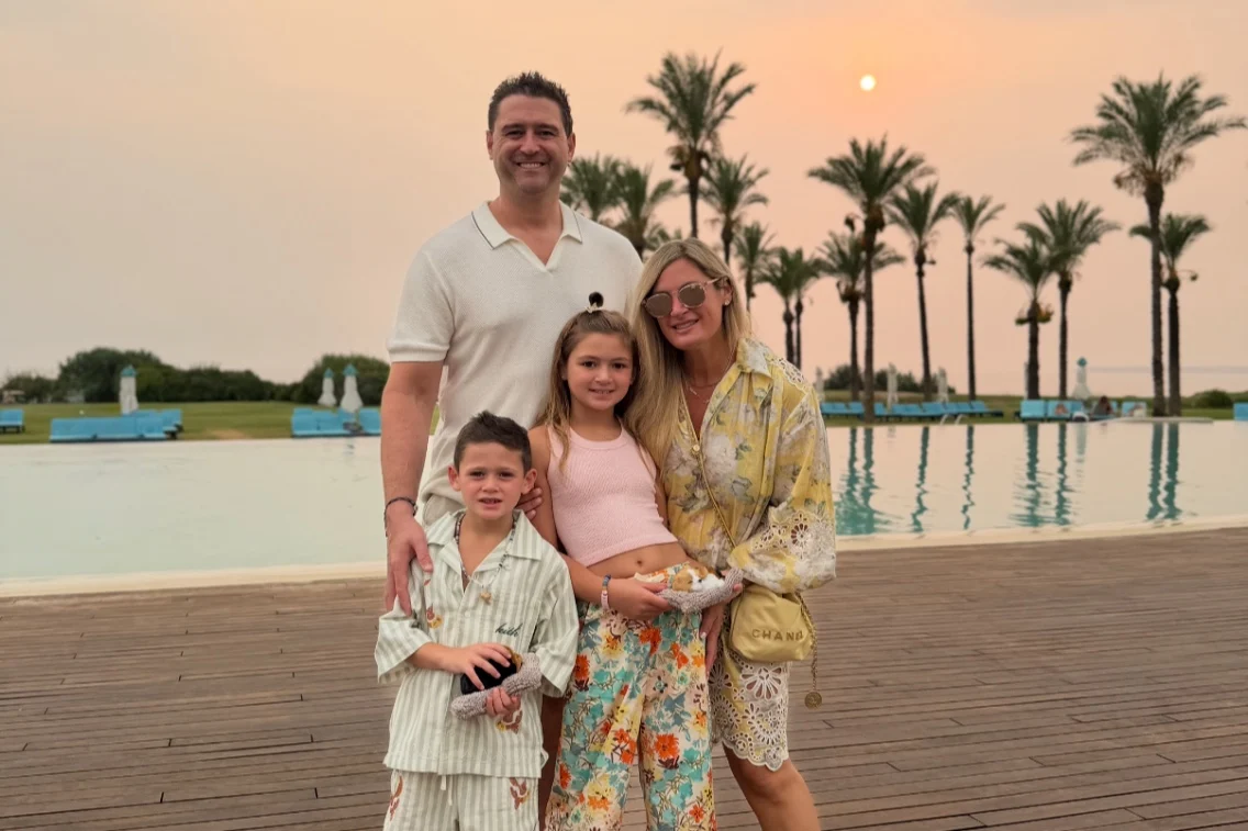 Family posing together near a pool with palm trees and a sunset backdrop at Rocco Forte's Verdura Resort.