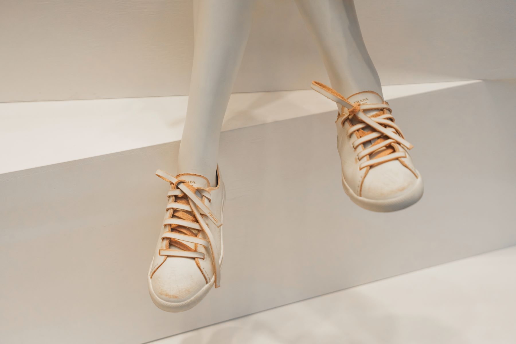 Distressed sneakers displayed on a mannequin, featuring a white leather exterior and beige laces, embodying the distressed-luxe trend.