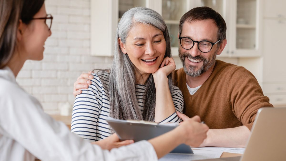 A couple smiles while engaging with a financial advisor who presents information on a tablet in a bright, modern setting.
