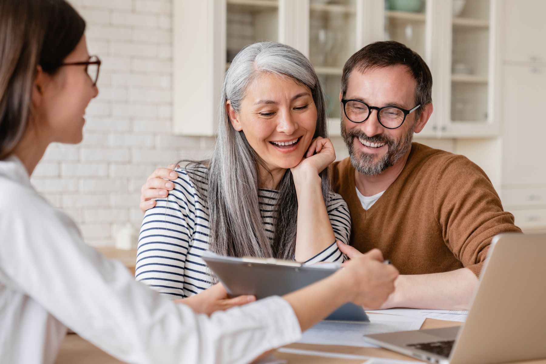 A couple smiles while engaging with a financial advisor who presents information on a tablet in a bright, modern setting.