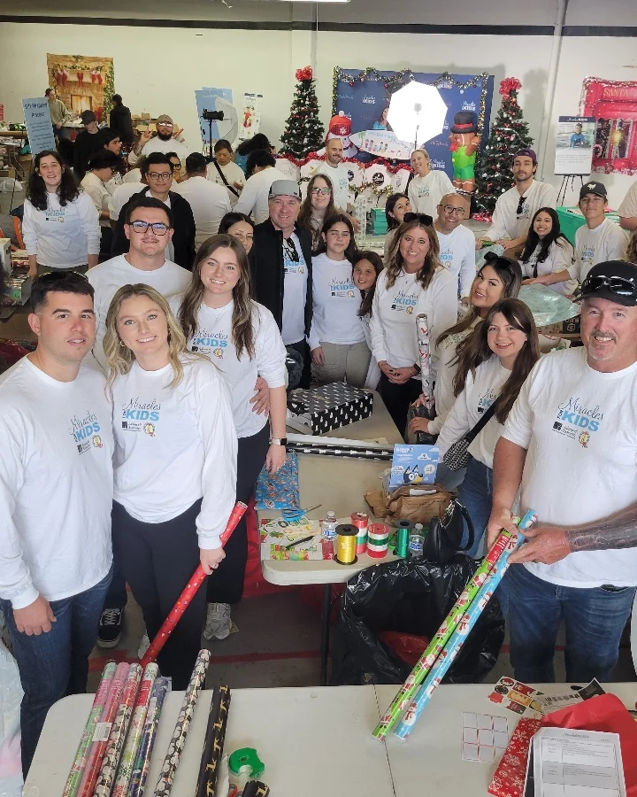 Volunteers gather at a festive location to wrap gifts for the Miracles for Kids Adopt-a-Family program, supporting families in need.