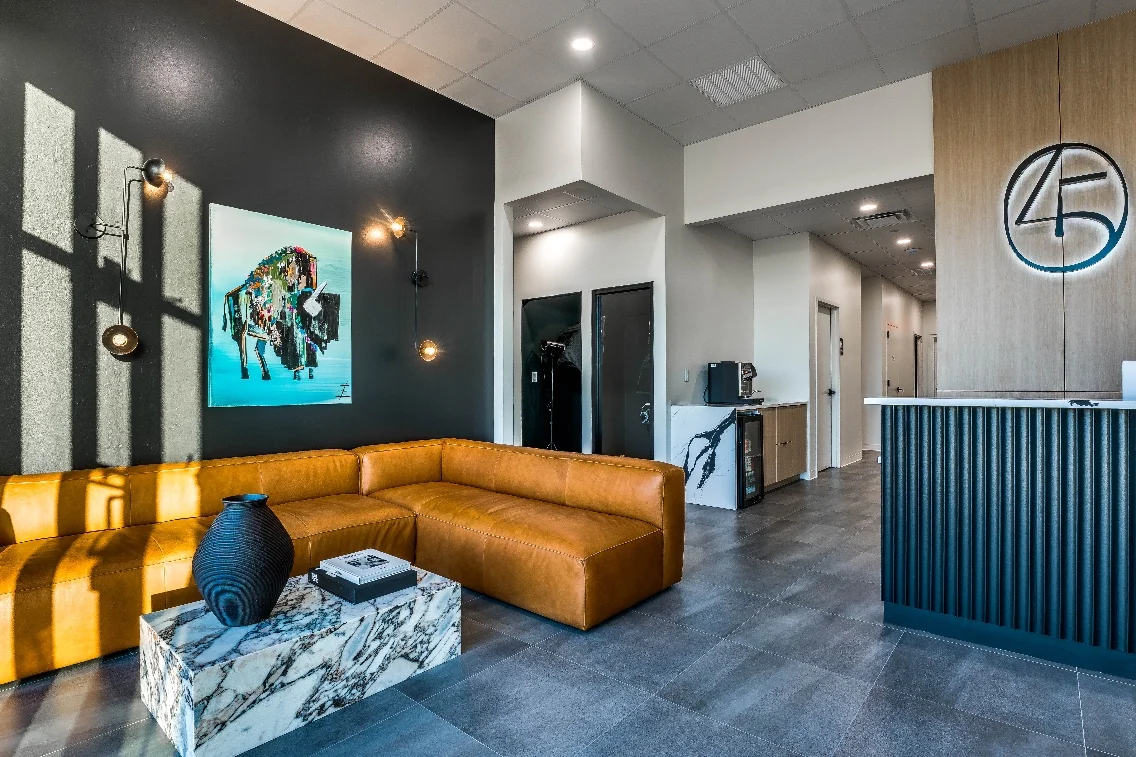 Modern dental office waiting area featuring a stylish brown couch, marble coffee table, and contemporary artwork on the wall.