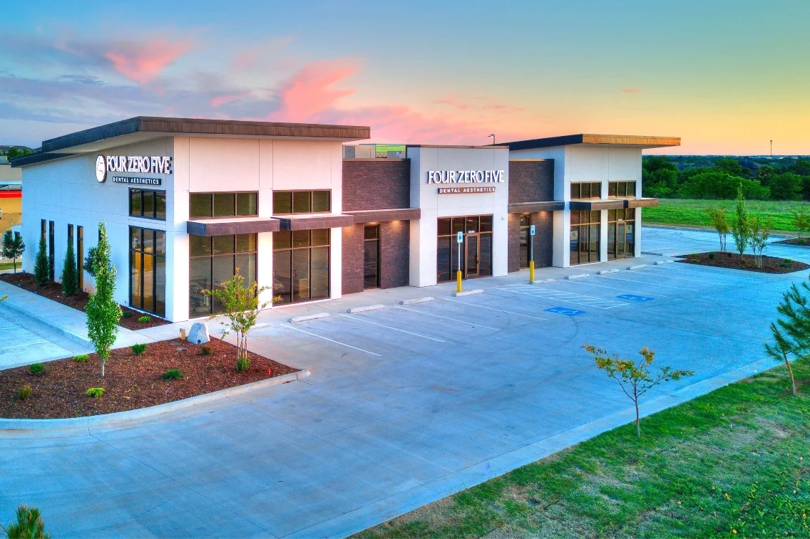 Modern dental clinic exterior with signage, landscaped surroundings, and a clear sky at dusk.