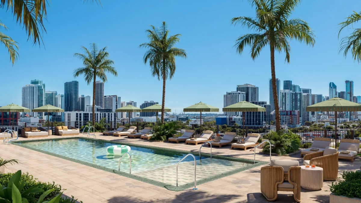 Rooftop pool area in Miami with palm trees, lounge chairs, and city skyline in the background under a clear blue sky.