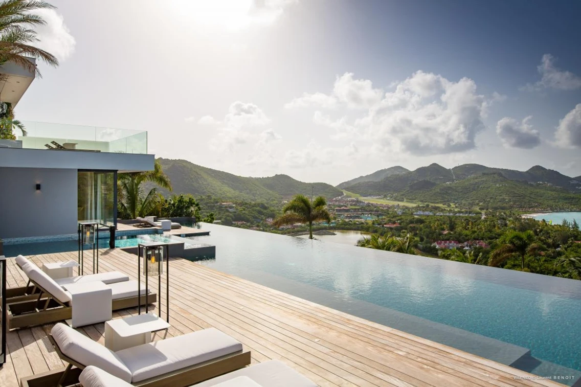 Infinity pool and lounging area with scenic mountain and ocean views at a luxury villa in St. Barts.