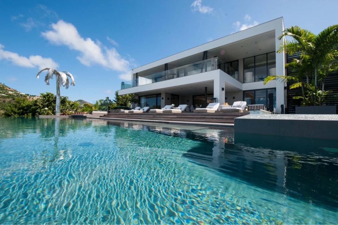 Luxury vacation rental in St. Barts featuring a pool, modern design, and ocean views surrounded by lush greenery.